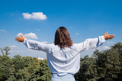 Rear view of woman with arms outstretched standing against sky