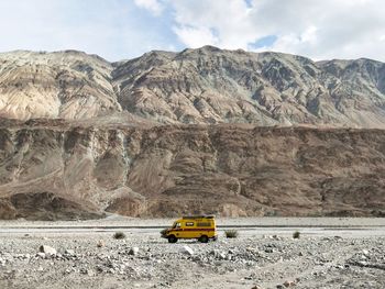 Yellow off-road vehicle on field against mountains against sky