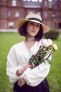 Portrait of a beautiful young woman in a hat , holding a bouquet of peonies in her hands