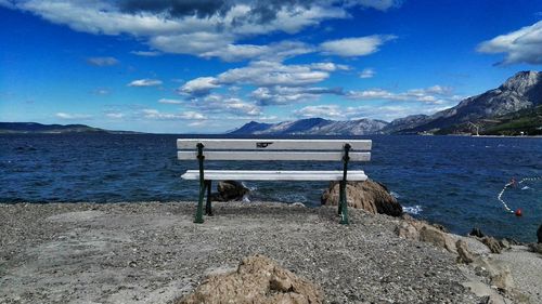 Empty bench at sea shore against sky