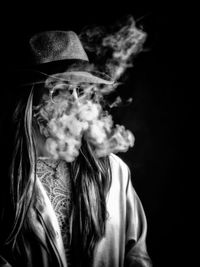 Young woman smoking against black background