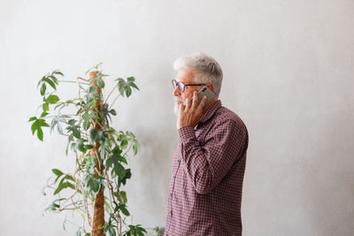Mature man talking on phone against wall