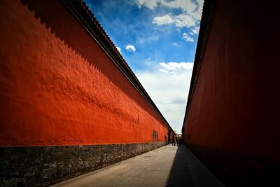 Walkway leading towards building against cloudy sky