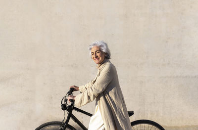 Smiling mature woman on bicycle by wall