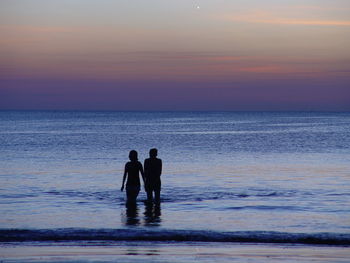 Silhouette men standing on beach against sky during sunset