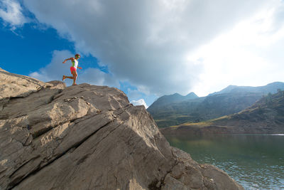 Man standing on rock by mountain against sky