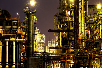 Low angle view of illuminated oil industry against sky at night