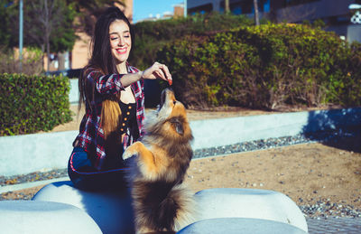 Beautiful young woman feeding dog sitting against blurred background