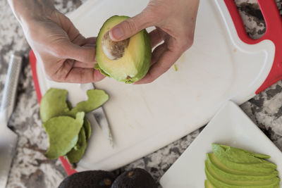 Cropped image of hands peeling avocado on cutting board