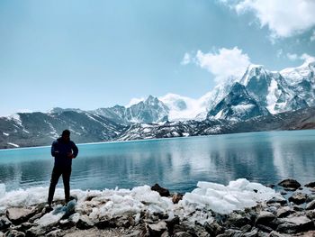 Rear view of man standing on snowcapped mountain against sky