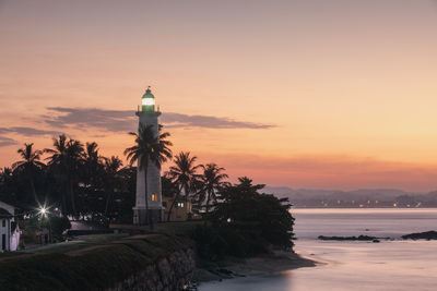 Lighthouse by sea against sky during sunset