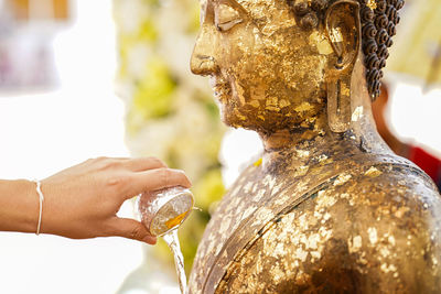 Cropped hand pouring water on buddha statue