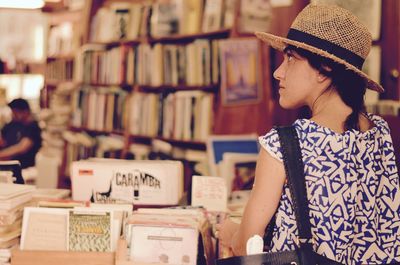 Rear view of young woman wearing hat standing by shelf in store