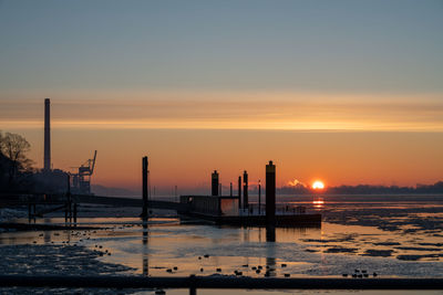 Silhouette wooden posts in sea against sky during sunset