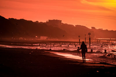 Woman walking at beach against orange sky