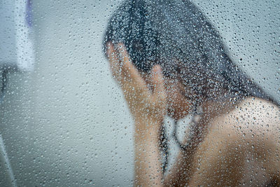 Woman taking shower seen through wet glass