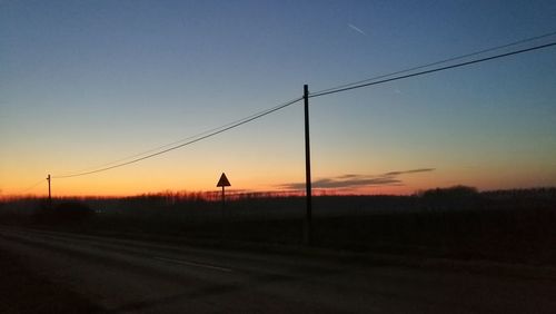 Silhouette electricity pylons on road against clear sky during sunset