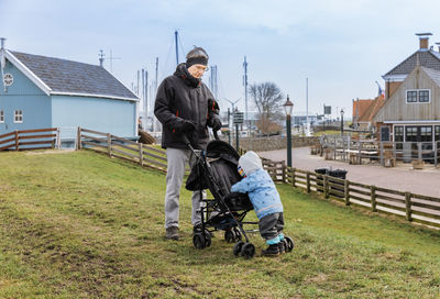 Grandfather and granddaughter with baby stroller on field in town