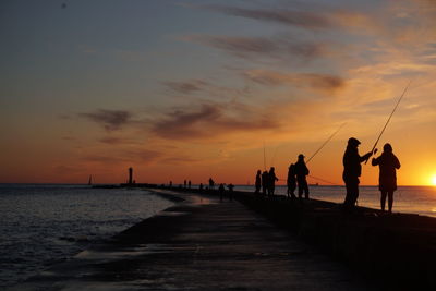 Silhouette people on beach against sky during sunset