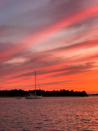 Sailboat sailing on sea against romantic sky at sunset