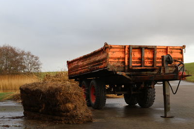 Hay stack by trailer on road against sky