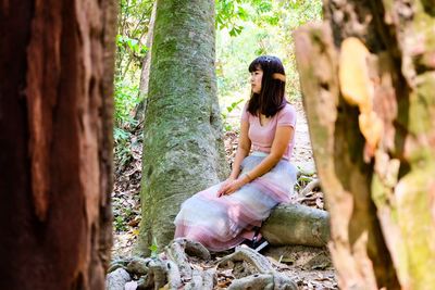  young woman looking away sitting on tree trunk in forest