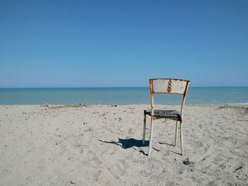 Rusty chair on beach against clear sky