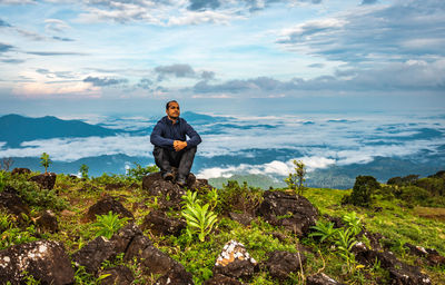 Man sitting on rock by sea against sky