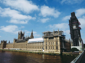 Buildings by river against cloudy sky