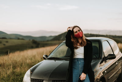 Woman standing by car on field against sky