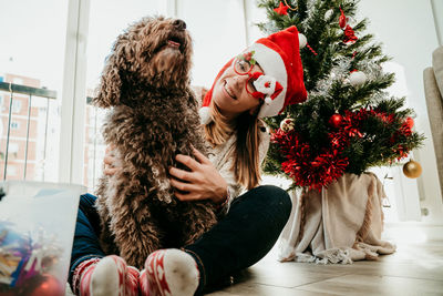 Full length of young woman sitting by christmas tree at home