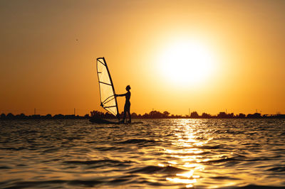 Silhouette person in sea against sky during sunset