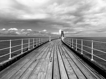 Wooden footbridge over sea against sky