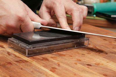 Cropped hand of person sharpening knife on table