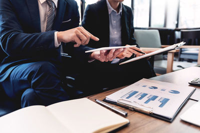 Midsection of businessmen discussing paperwork on desk