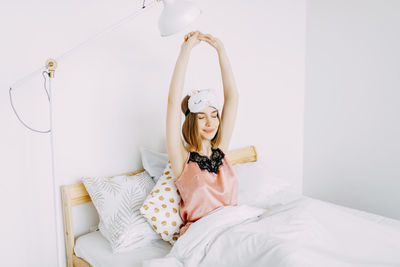 Portrait of young woman sitting on bed against white wall