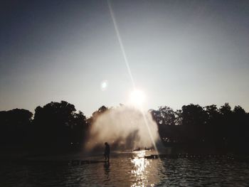 Silhouette people splashing in lake against sky