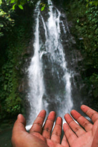 Cropped image of person hand on waterfall