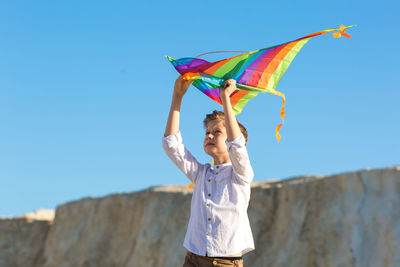 A boy in a white shirt with a kite in his hands plays mountains.