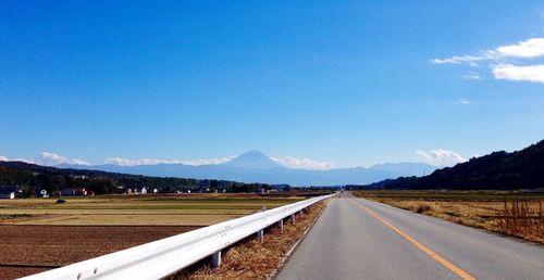 Empty road amidst landscape against blue sky