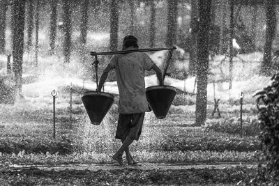 Rear view of man walking on field and watering the plants