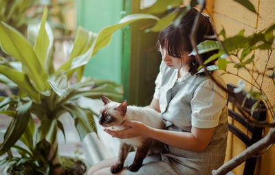 Woman with cat sitting by plants on chair