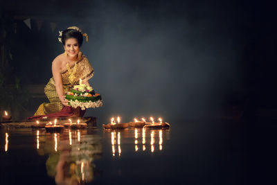 Portrait of young woman in traditional clothing kneeling by lake at night