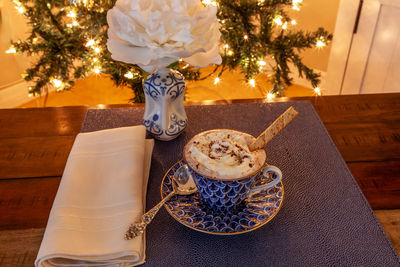 Cup of hot chocolate in a fancy bone china cup with gold and a silver spoon in front of a christmas