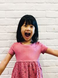 Portrait of cute girl with mouth open standing against brick wall