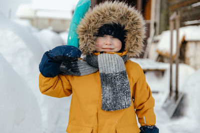 Image of a happy five-six-year-old kid in an orange jacket looks into the camera and smiles. 