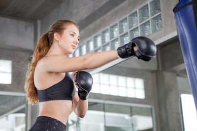 Low angle view of young female boxer punching bag in gym