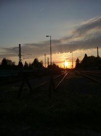 Silhouette railroad tracks on field against sky during sunset