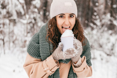 A smiling girl with a green scarf in winter in the forest there is snow from a mug
