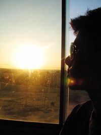 Man standing by window at sunset